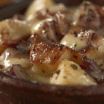 Southern smothered potatoes in a cast iron skillet topped with creamy gravy and caramelized onions.