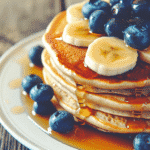 Stack of blueberry banana oatmeal pancakes with syrup and fruit