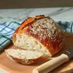 Freshly baked artisan sourdough bread on a rustic wooden board with a crisp, golden crust and flour dust around.