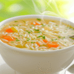 Warm pastina soup with egg in a white bowl on rustic table