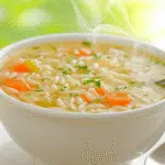 Warm pastina soup with egg in a white bowl on rustic table