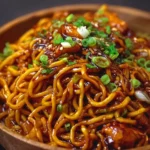 Plate of sticky garlic chicken noodles garnished with green onions