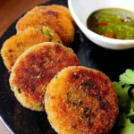 A plate of crispy Veg Cutlets garnished with herbs and served with dipping sauce.