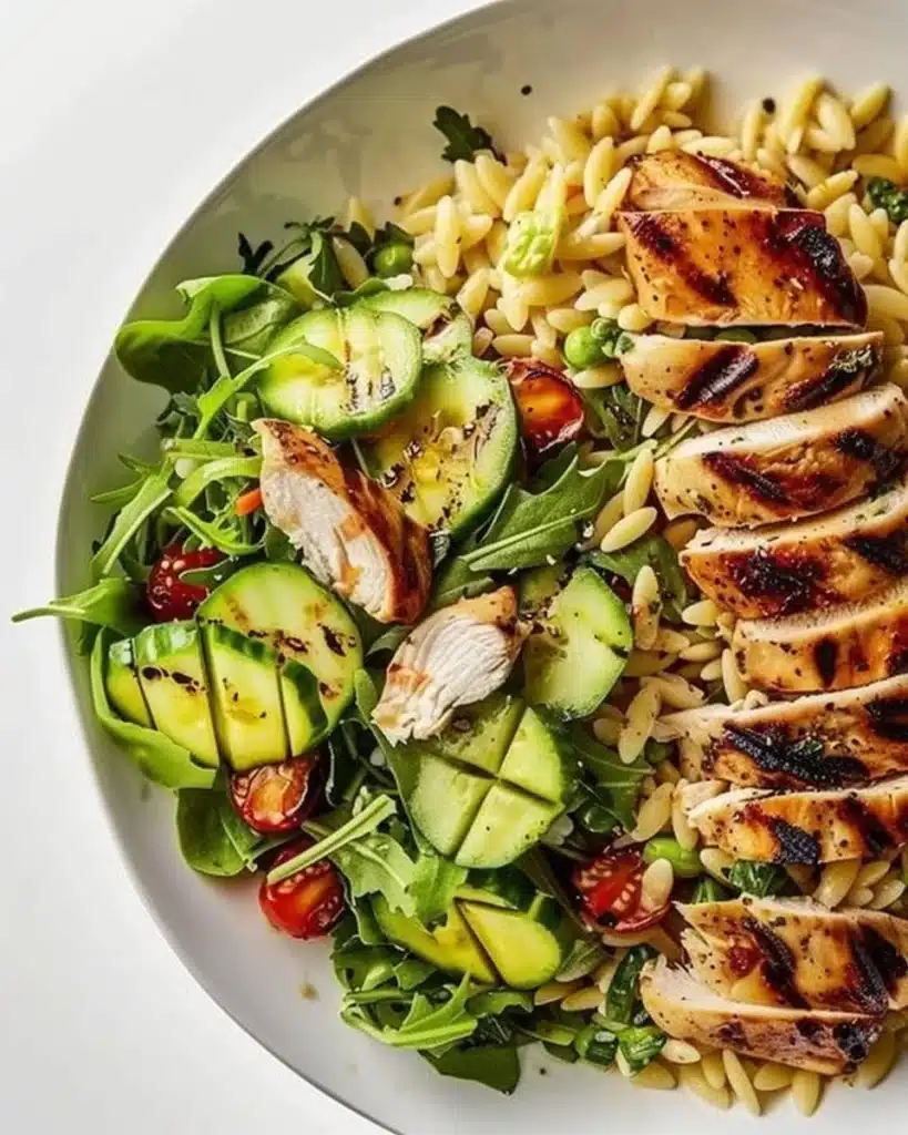 Grilled chicken orzo salad served in a bowl with fresh vegetables.