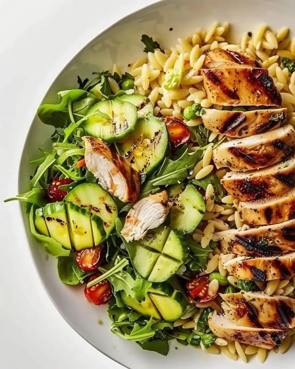 Grilled chicken orzo salad served in a bowl with fresh vegetables.