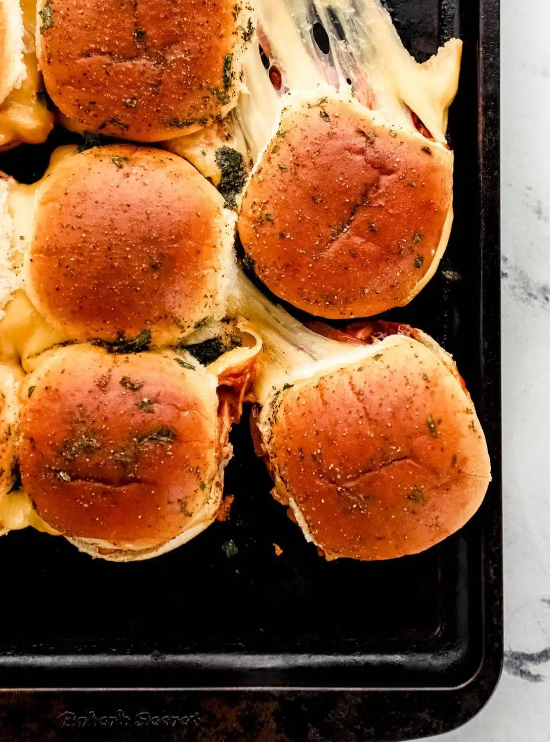 BBQ Chicken Sliders served with pickles and coleslaw on a wooden platter.